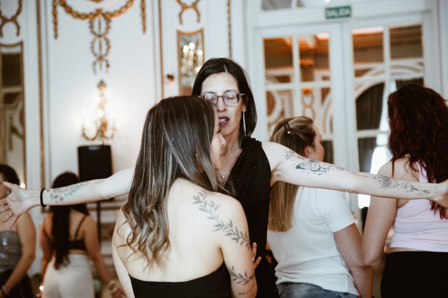Mujeres en círculo con los brazos enlazados, en un salón de Buenos Aires con molduras doradas.